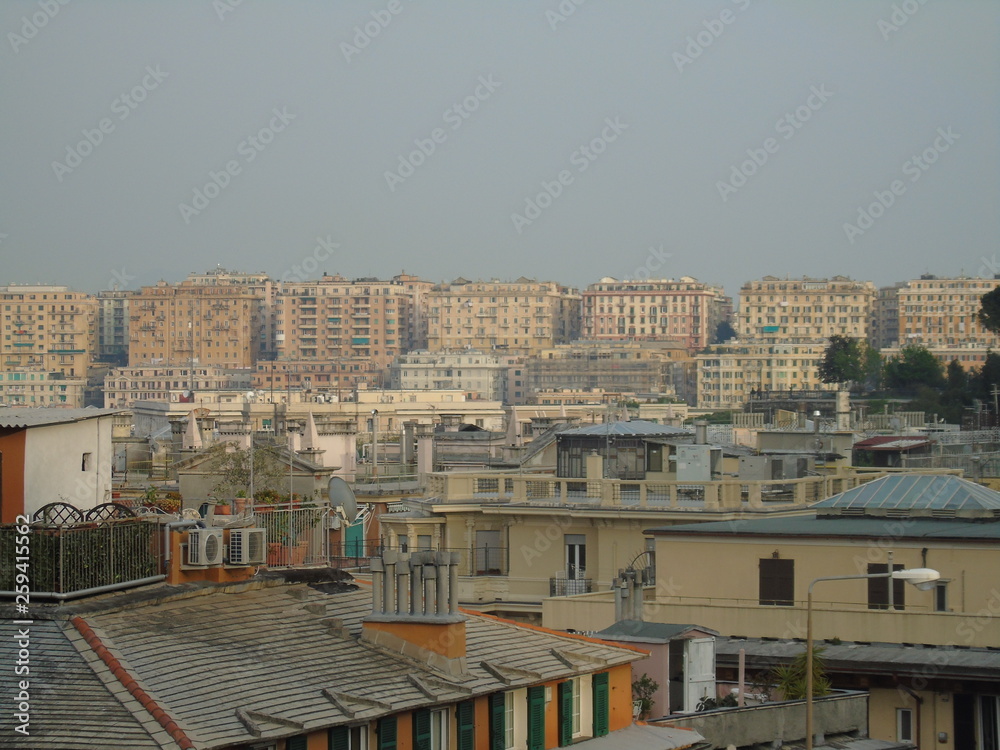 Fototapeta premium Genova, Italy - 04/02/2019: An amazing caption of the city of Genova from the hills in winter days, with a great grey sky, some tall skyscrapers and beautiful old buildings