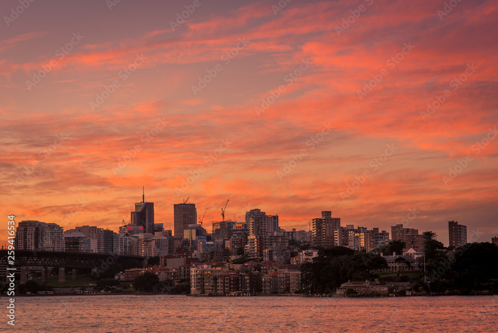 A sunset panoramic of buildings and skyscrapers at Sydney Harbour, on the far side of the bridge