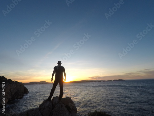 Joven de pie mirando el amanecer sobre el mar en el horizonte sobre una montaña. Concepto de viajar, descubrir, naturaleza, superación y  disfrutar de la libertart