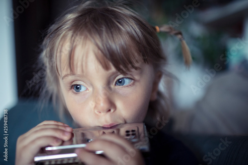 Close up of blond girl with gray eyes playing harmonica at home