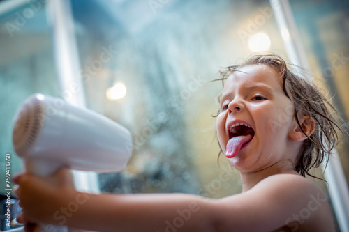 Blond girl playing with hair dryer in bathroom