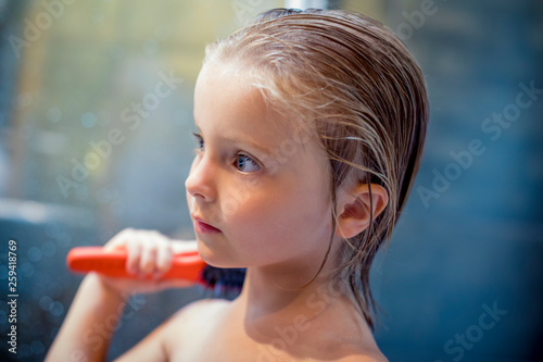 Blond girl combing her wet hair in bathroom photo