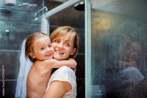 Smiling blond mother and daughter standing in bathroom