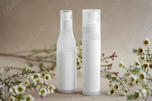 Two white cosmetic bottles on a beige background decorated with flowers