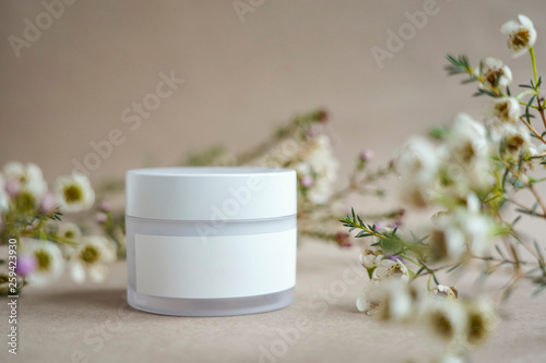 White  round cosmetic jar on a beige background decorated with white flowers
