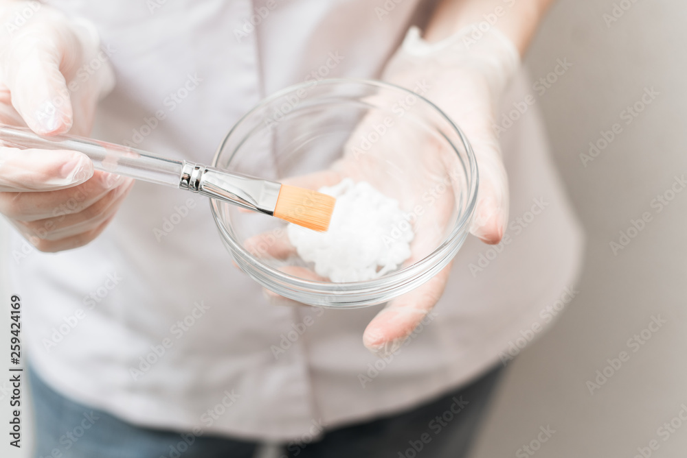 advertising campaign for cosmetology. The girl in a white medical gown and gloves mixes the mask in a bowl on a white background. advertising campaign for cosmetology. The girl in a white medical gown and gloves mixes the mask in a bowl on a white background.
