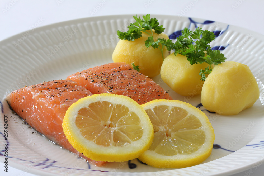 Salmon fillet with potatoes, lemon slices and parsley served on a plate. Close up stock photo. Salmon fillet with potatoes, lemon slices and parsley served on a plate. Close up stock photo.