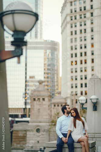beautiful long-haired girl in summer dress with her handsome husband in white shirt and pants sitting in sunny Chicago
