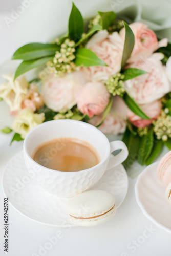 Elegant sweet dessert macarons, cup of coffee and pastel colored beige flowers bouquet