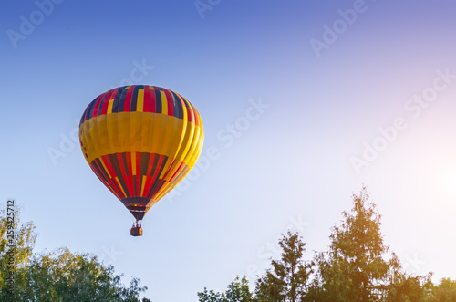 Colorful hot air balloon is flying in the blue sky above the trees