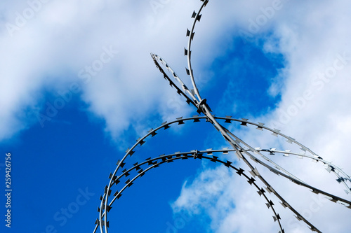 Barbed wire fence with blue sky and white clouds.