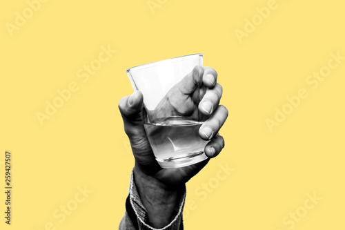 Concept of drought, running out of water, dry summer, global warming. Hand holding an empty glass of water with just one drop falling down. Black and white subject with yellow background photo