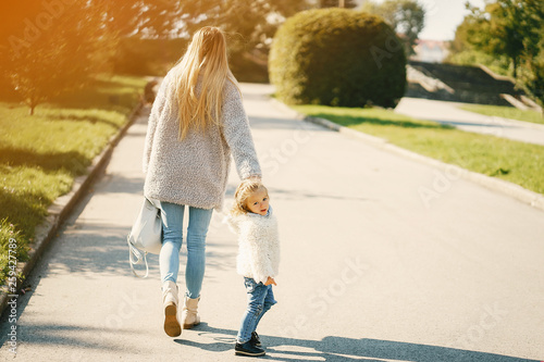 Fototapeta Naklejka Na Ścianę i Meble -  young blonde mother walking in the park with her toddler daughter on a sunny day wearing coats