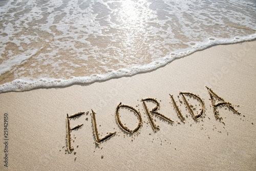 Simple Florida American holiday getaway message written in smooth sand with an incoming wave on a tropical beach