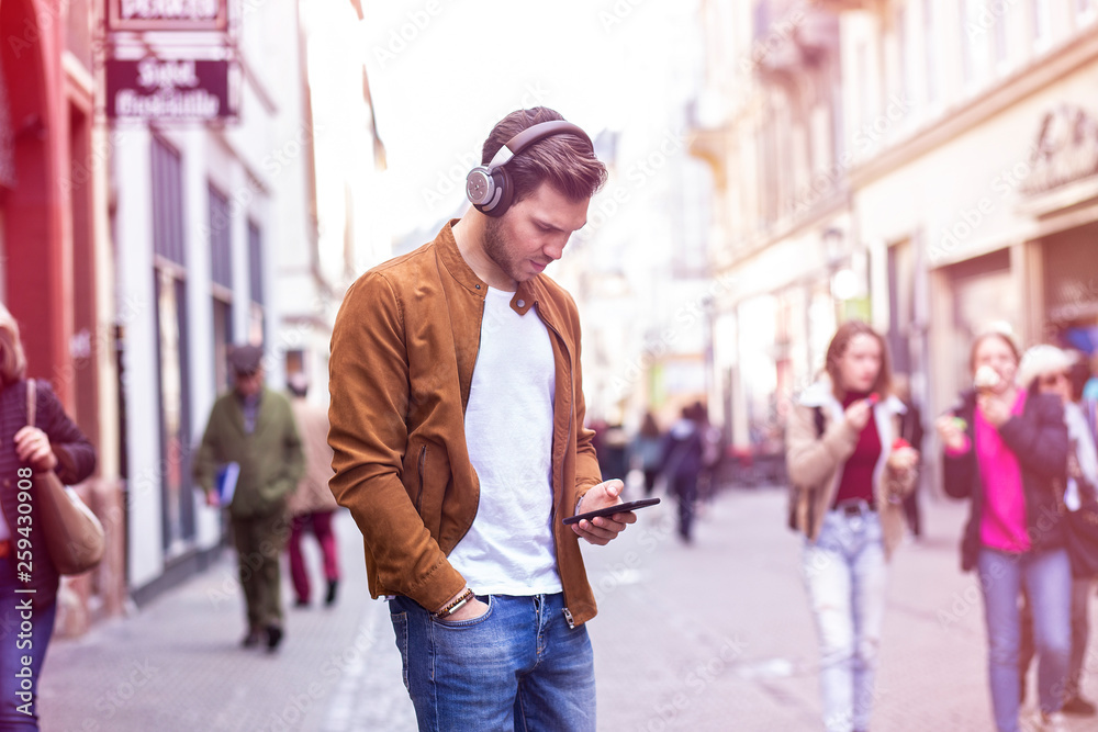 Young Adult Man Listening Music on Smartphone and Headphone on The Street at Summer Time 