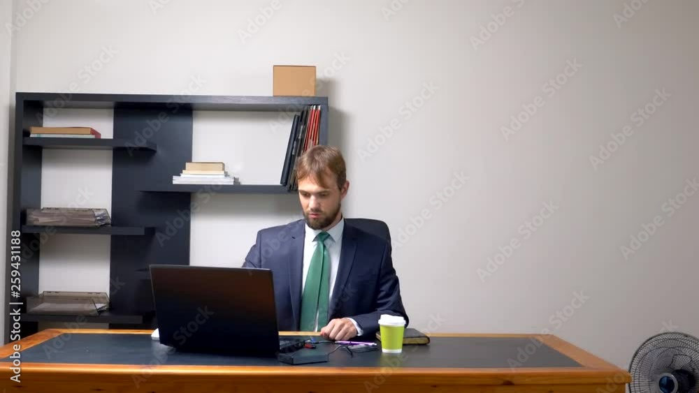a man in a suit works at a desk in the office on a laptop and drinks coffee from a disposable cup. copy space a man in a suit works at a desk in the office on a laptop and drinks coffee from a disposable cup. copy space