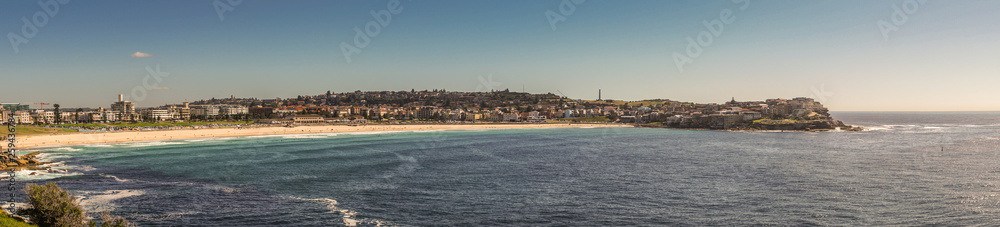 Sydney, Australia - February 11, 2019:  Panorama shot of sandy Bondi beach and its north shore with housing and nature reserves. Blue water and sky.