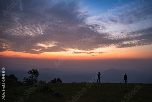Photographer man standing on hill with sunrise landscape mountain fog mist colorful sky beautiful clouds in the morning silhouettes