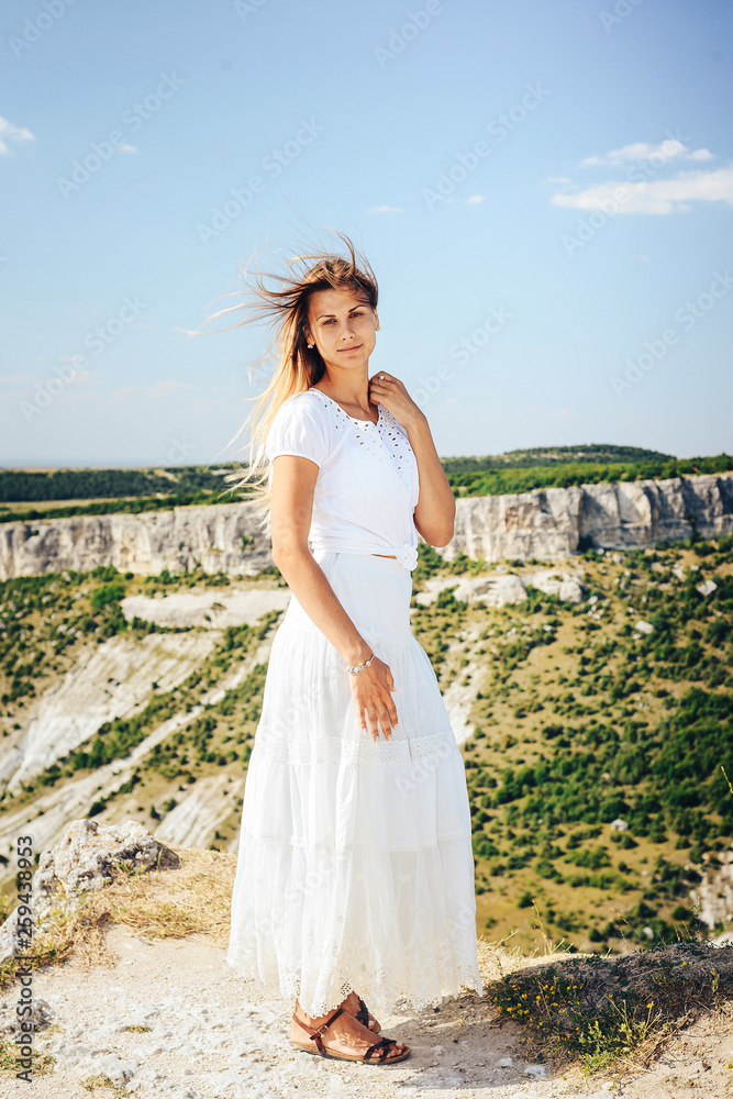 Attractive girl in a snow-white dress with flowing hair, posing on top of the mountain.