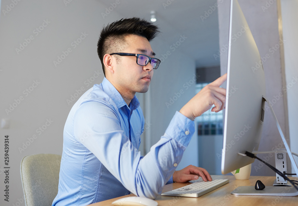 Naklejka premium Young asian blockchain professional wearing shirt and glasses working while sitting in front of desktop computer at coworking office