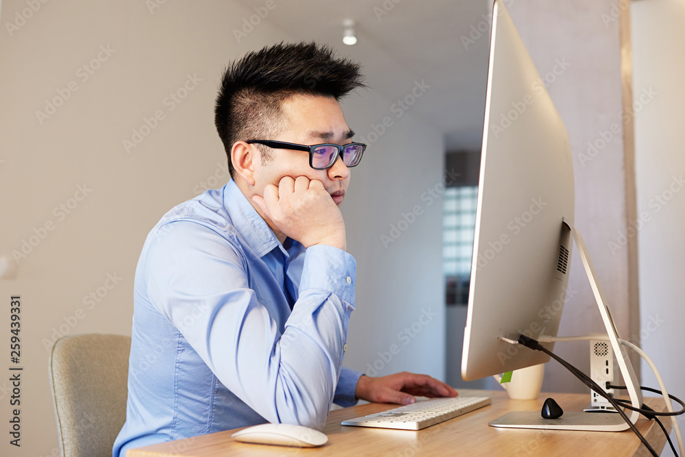 Obraz premium Young asian designer professional wearing shirt and glasses working while sitting in front of desktop computer at coworking office