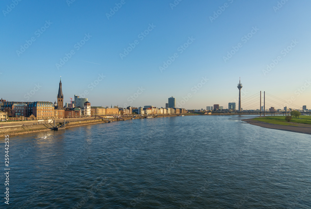 Outdoor panoramic sunny scenic cityscape view of Düsseldorf city, Germany, with promenade walkway on waterfront through old town and downtown, view from the bridge over Rhine River. 