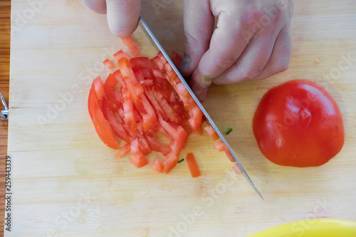 cooking, food and home concept - close up of male hand cutting tomato on cutting board at home photo