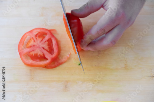 cooking, food and home concept - close up of male hand cutting tomato on cutting board at home photo