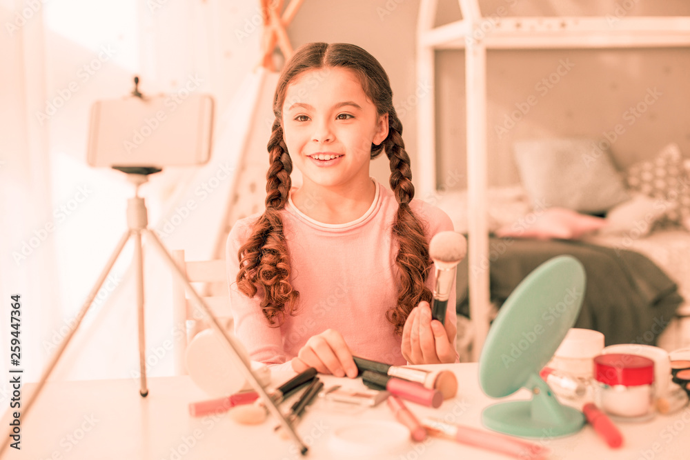 Obraz premium Delighted nice girl sitting in front of her smartphone