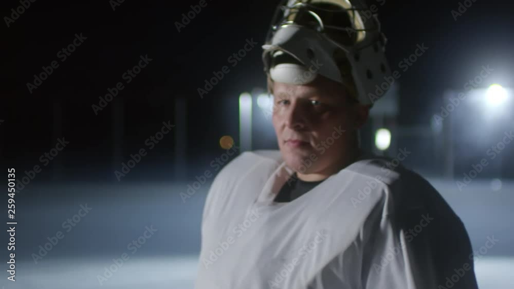Zoom out portrait of middle-aged ice hockey player standing on rink and looking at camera, then putting on helmet and starting the game Zoom out portrait of middle-aged ice hockey player standing on rink and looking at camera, then putting on helmet and starting the game