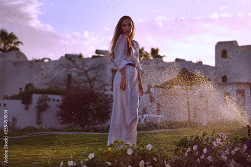 Natural beauty. Beautiful woman with long hair in traditional white dress among summer green garden with colorful flowers.