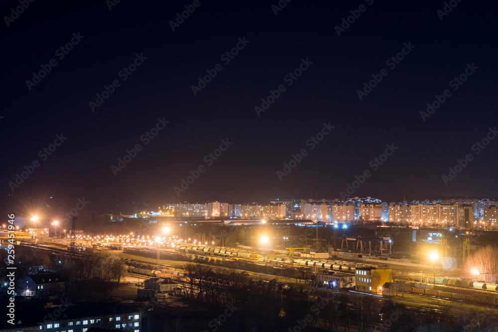 Bright railway station at night against the backdrop of the outskirts of the city. Freight trains.