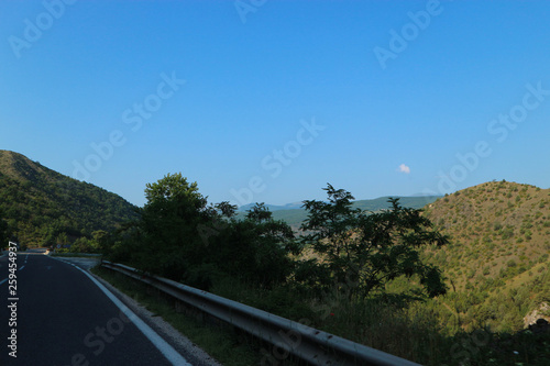 Road to vacation mountains, valley, green trees and blue sky photo