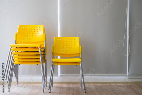 Yellow stacking plastic chairs for meeting or workshop in front of gray background.