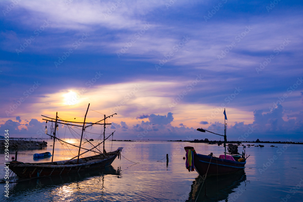 Fishing boat in the sea, sunset and silhouettes of wooden boats
