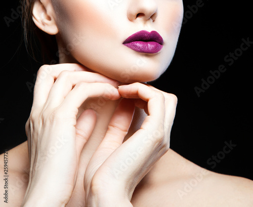 Part of beauty fashion model woman studio portrait, bright purple lips make-up, clean skin, hands near neck. Black background