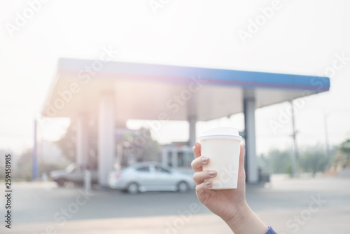 Paper coffee cup in hand the background is gas station
