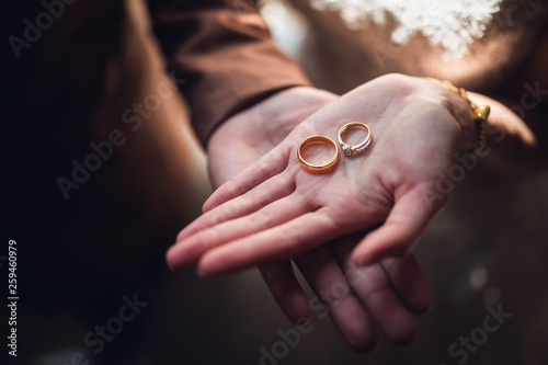 Closeup photo of bride and groom holding golden wedding rings on hands - Image