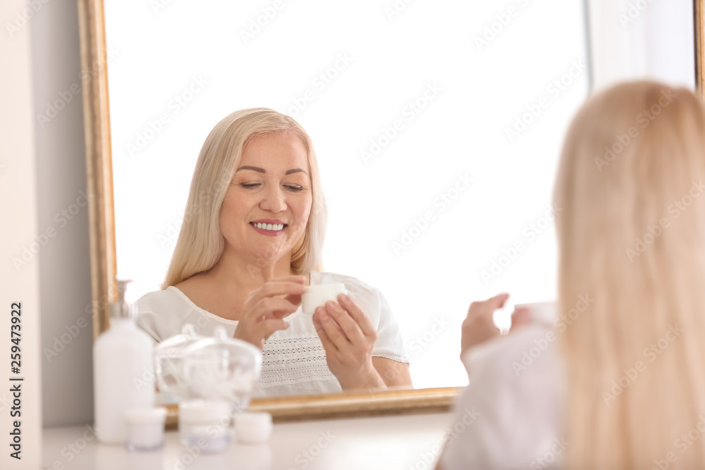 Mature woman applying facial cream at home Mature woman applying facial cream at home