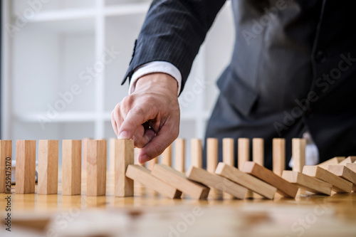 Wooden game strategy, Businessman hand stopping falling wooden dominoes effect from continuous toppled or risk, strategy and successful intervention concept for business
