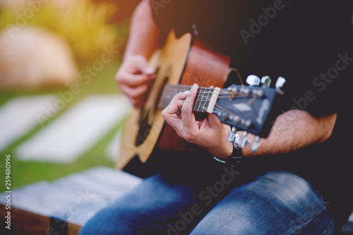 Picture of a guitarist, a young man playing a guitar while sitting in a natural garden,music concept