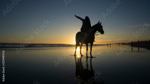 silhouette of muslim women who are riding horses on the beach with the atmosphere of the sunset