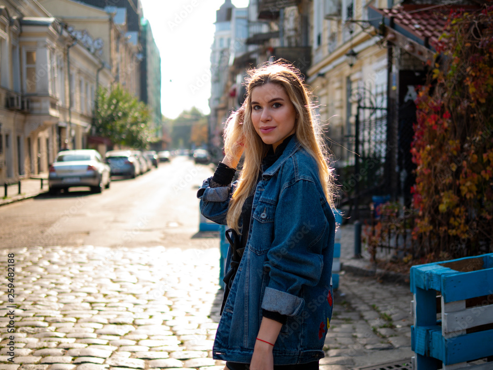 beautiful blonde girl stands in an old alley in a denim jacket