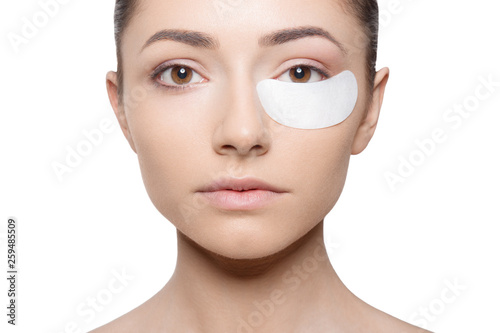 Woman applying her plaster under her eye during make up, isolated on white background. Horizontal view.