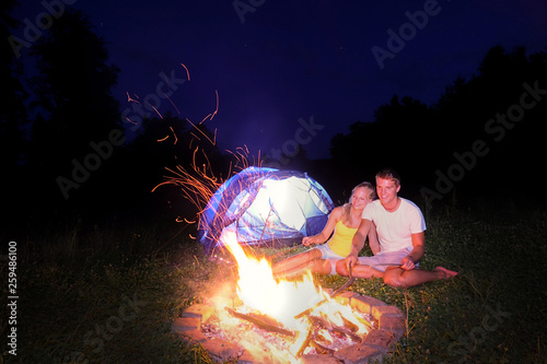 Couple enjoying a camping trip and roasting sausages over the big campfire.