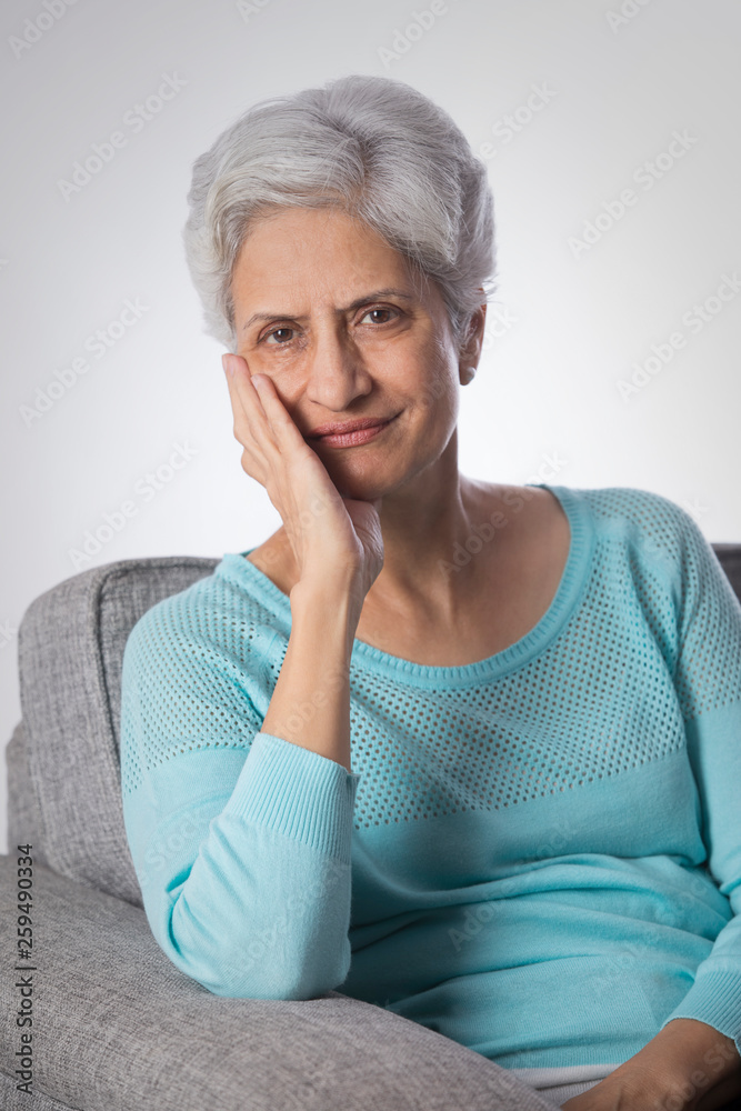 Portrait of senior woman thinking sitting on sofa with hand on chin Portrait of senior woman thinking sitting on sofa with hand on chin