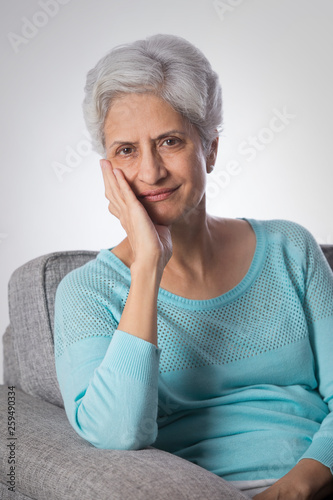 Portrait of senior woman thinking sitting on sofa with hand on chin 