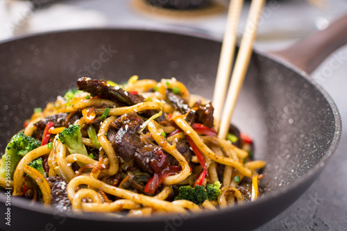 Fotografia, Obraz Udon Stir-Fry Noodles with Beef and Vegetables in Wok Pan on Dark Background