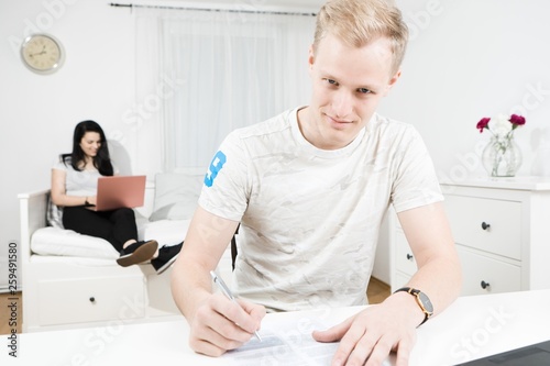 Blond man writing at desk and attractive woman typing on pinky notebook in the background