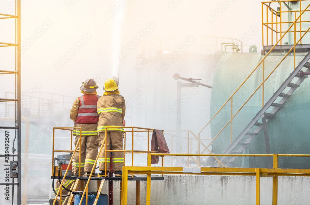 professional firemans brave buddy team assistance in yellow fire fighter uniform holding fire hose nozzle fighting with fire flame in the industrial factory